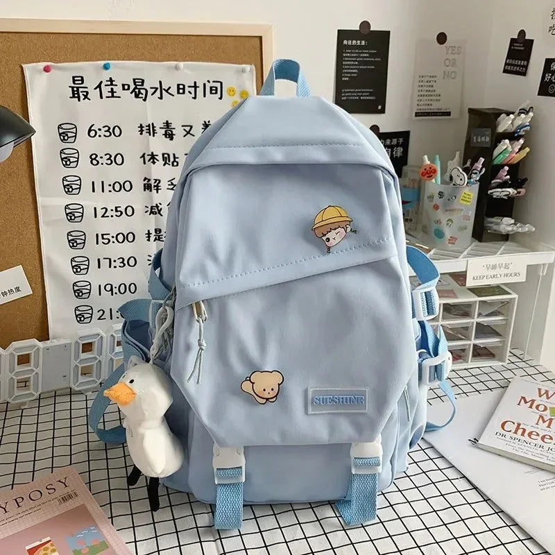 Light blue cute backpack with cartoon patches and a white duck keychain on checkered table