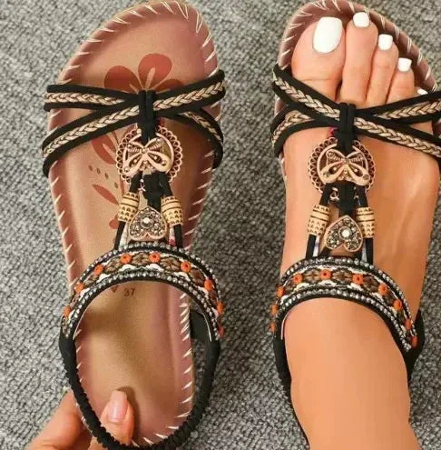 Stylish black sandals with intricate beaded and butterfly decorations worn on feet with white pedicure