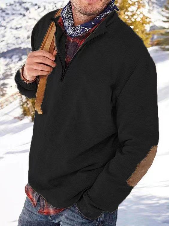 Man wearing a black quarter-zip pullover with brown elbow patches and a blue bandana, standing outdoors in snowy landscape