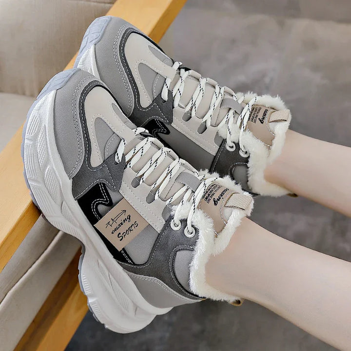 Grey and white fur-lined sports sneakers with thick soles and patterned laces on feet