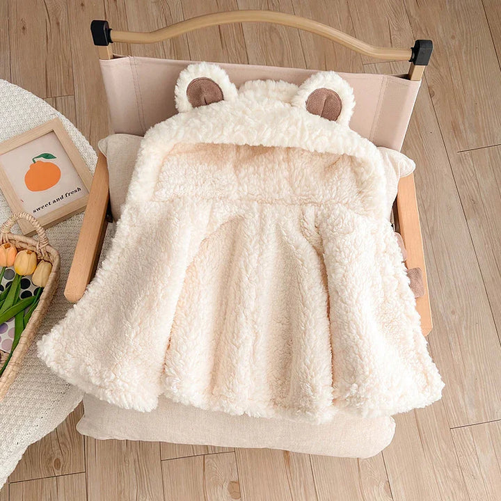 Soft cream-colored baby fleece jacket with bear ears hood on wooden chair