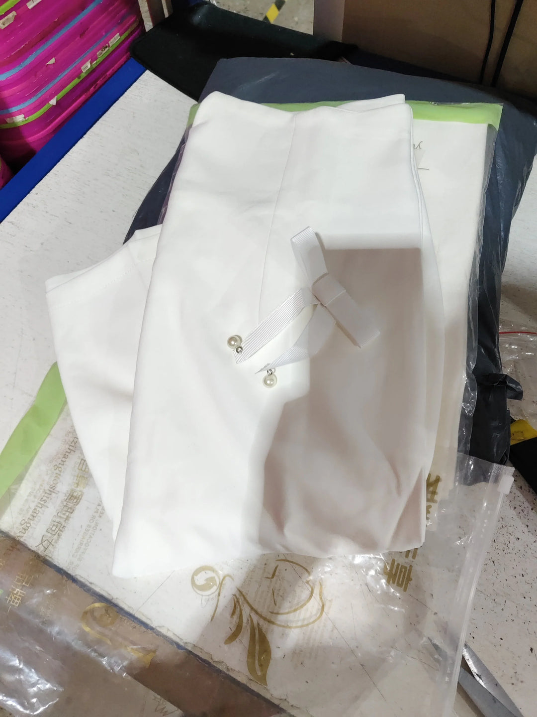 Folded white fabric with ribbon and pearl accessory on cluttered table surface