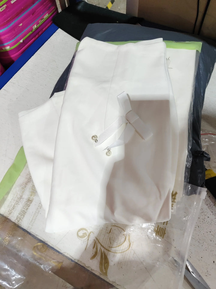 Folded white fabric with ribbon and pearl accessory on cluttered table surface