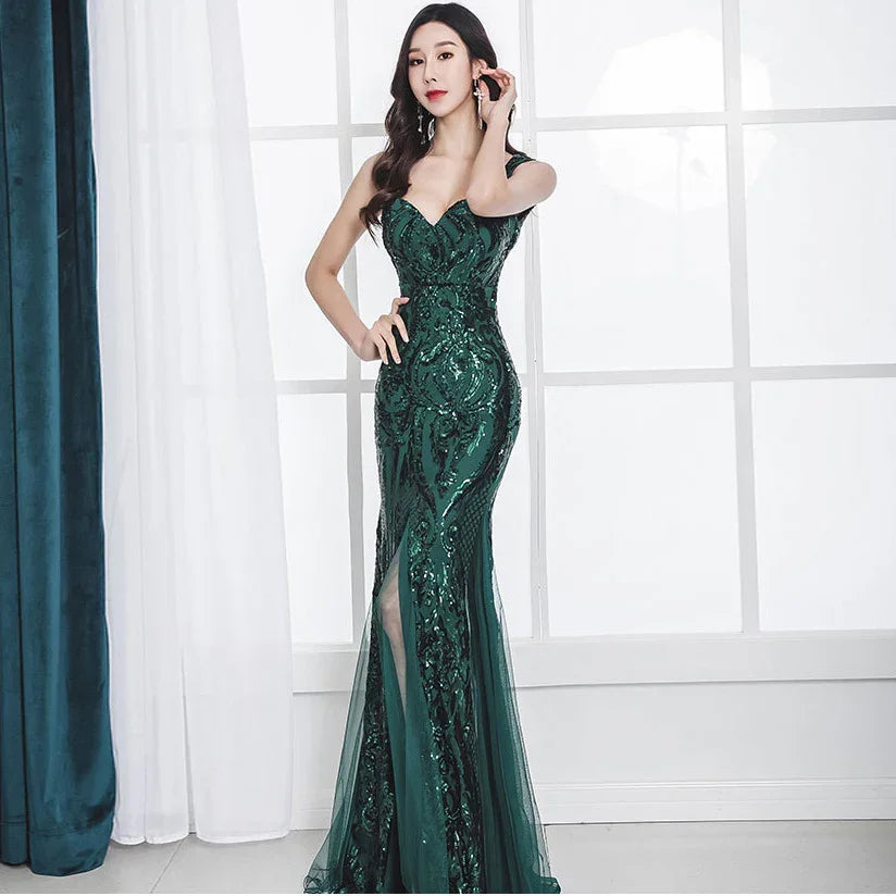 Woman in elegant dark green sequined evening gown with slit, posing by bright window and curtains