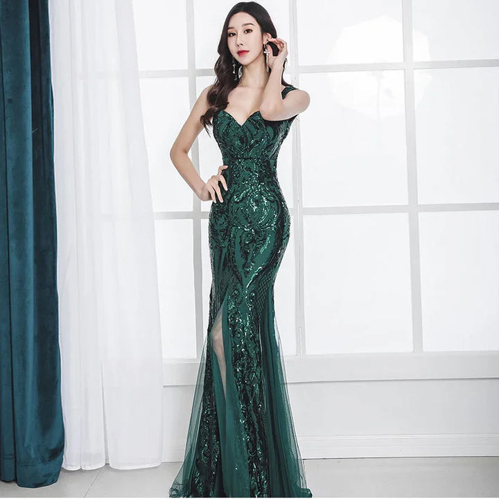 Woman in elegant dark green sequined evening gown with slit, posing by bright window and curtains