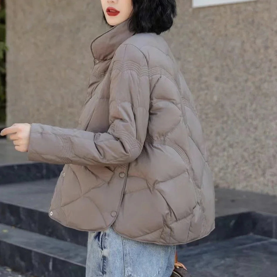 Woman wearing a taupe quilted puffer jacket with high collar and light blue jeans outdoors