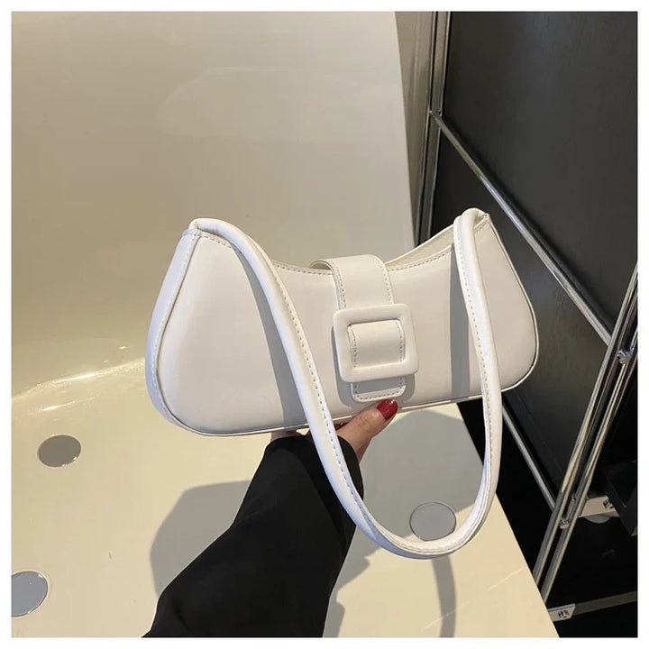 White leather shoulder bag with a square buckle detail held against a neutral background