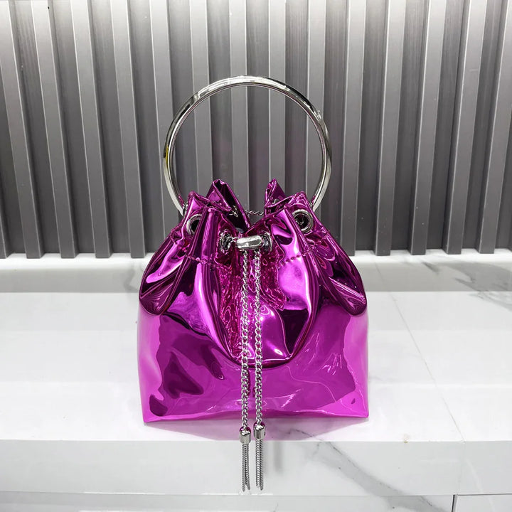 Shiny metallic purple handbag with silver ring handle and drawstring tassels on marble surface