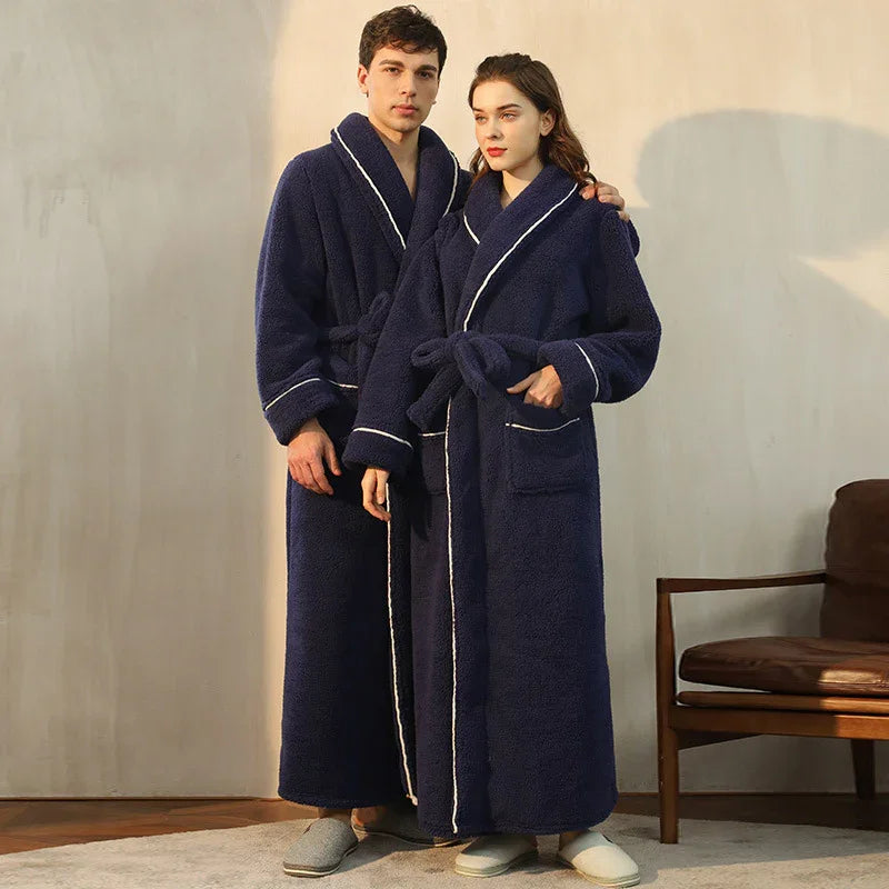 Man and woman wearing cozy navy blue fleece bathrobes with white piping, standing indoors near wooden chair