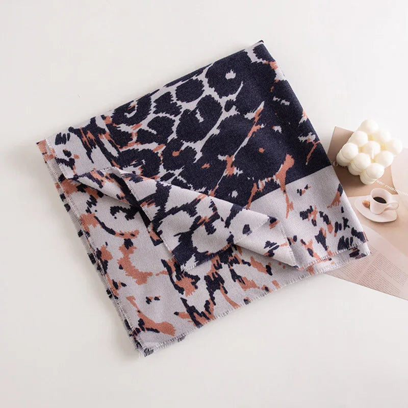 Folded leopard print scarf with black, gray, and brown colors on white surface next to decorative candle and coffee cup