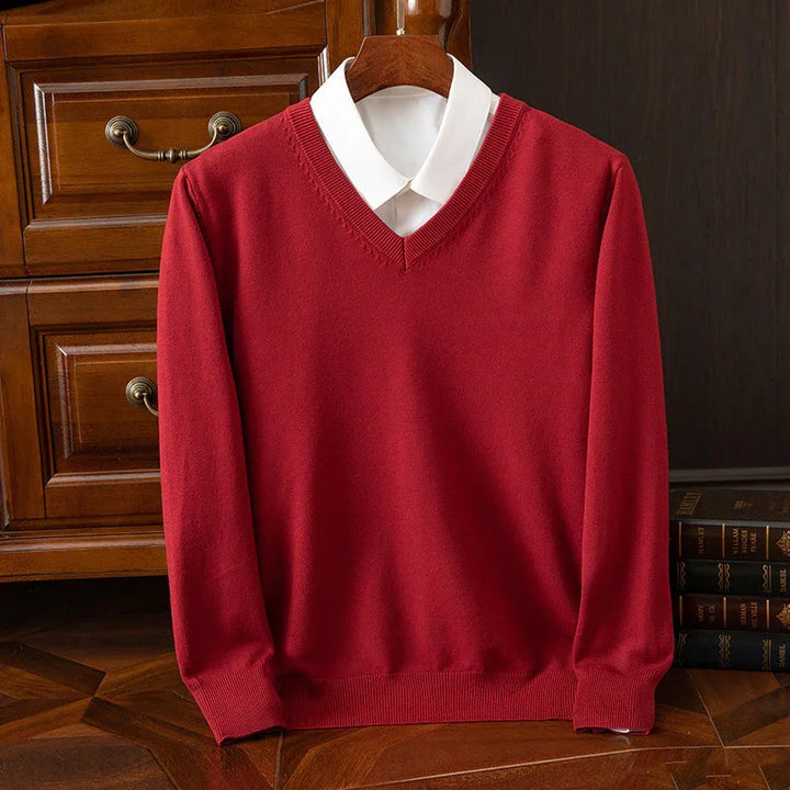 Red V-neck sweater layered over white collared shirt on wooden hanger against wooden furniture
