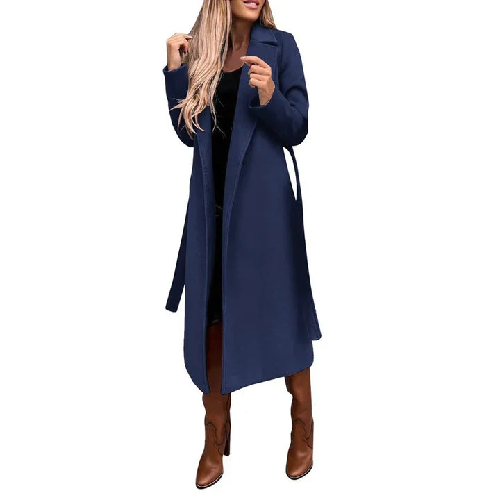 Woman wearing long navy blue trench coat with brown knee-high boots on white background