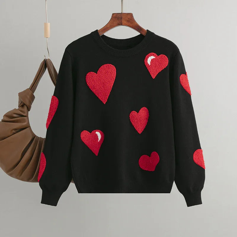 Black sweater with red textured heart patches hanging on wooden hanger with brown ruched handbag
