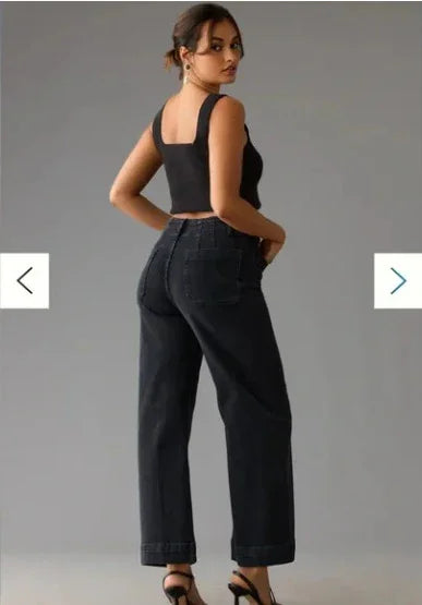 Woman wearing black sleeveless crop top and high-waisted black wide-leg jeans with heels on gray background