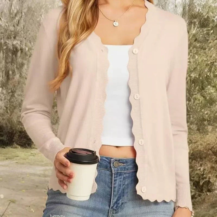 Woman wearing beige scalloped button cardigan, white crop top, blue jeans, holding coffee cup outdoors