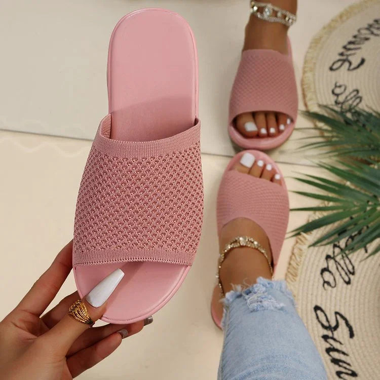 Pink knit slide sandals with open toes worn with gold anklets and white nail polish