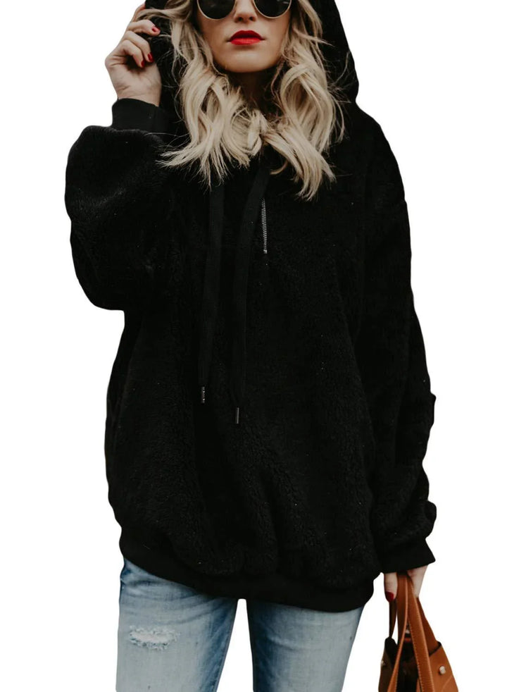 Woman wearing black fleece oversized hoodie with hood and light blue distressed jeans holding brown handbag