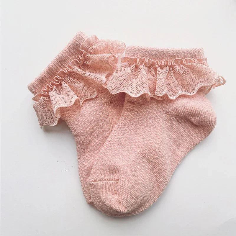 Soft pink baby socks with delicate lace ruffles on white background, cute infant footwear