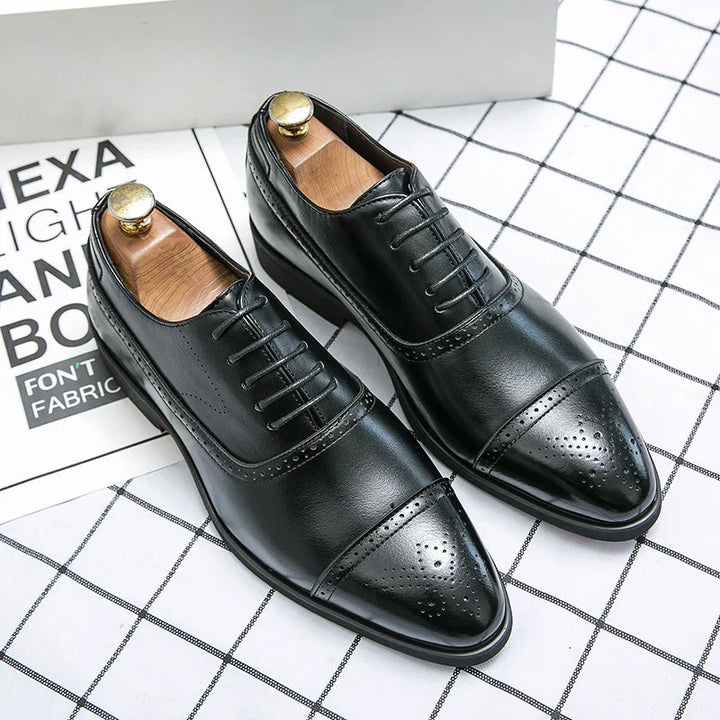 Pair of black leather men's dress shoes with brogue detailing and wooden shoe trees on checked surface