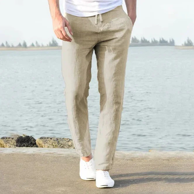 Man wearing beige linen pants and white sneakers walking by a lakeside on a sunny day