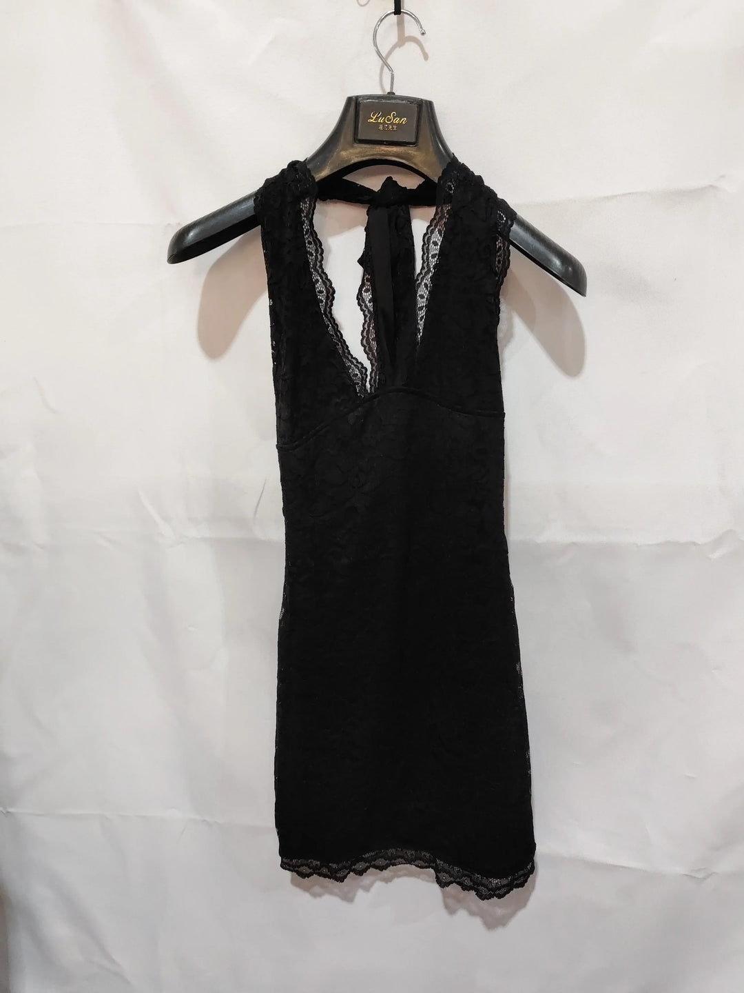 Black lace sleeveless dress with deep V-neckline hanging on LuSan branded hanger against white background