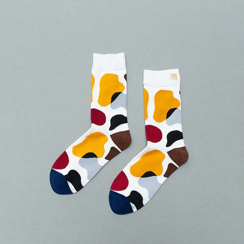 Pair of white socks with colorful abstract blotches in yellow, red, black, brown, grey, and blue on gray background