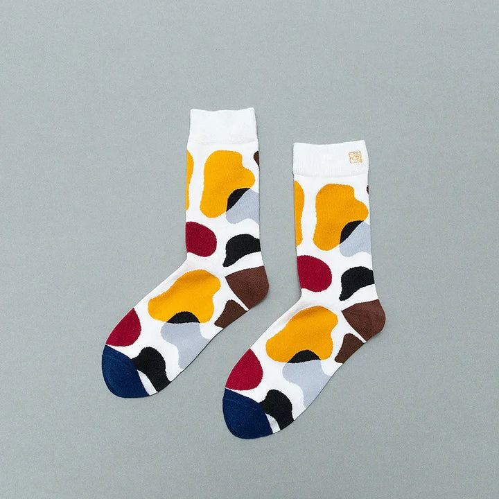 Pair of white socks with colorful abstract blotches in yellow, red, black, brown, grey, and blue on gray background