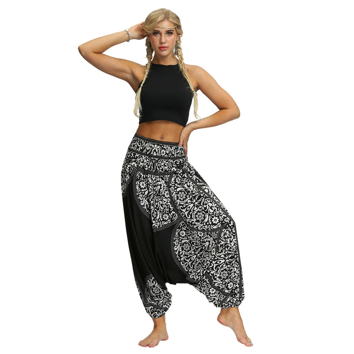 Young woman in black crop top and black white patterned harem pants posing barefoot on white background