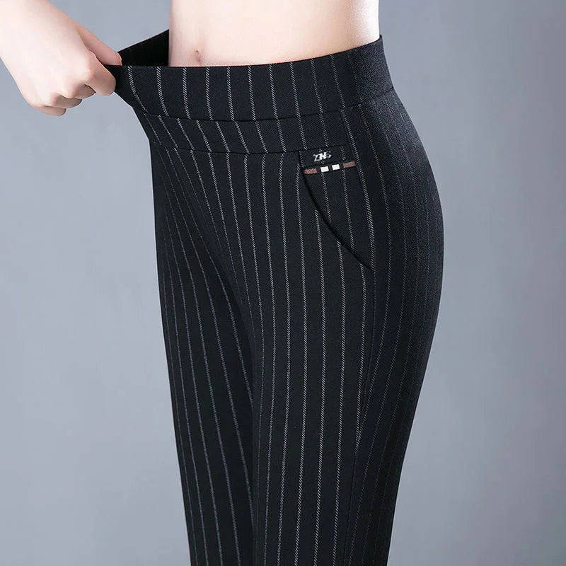 Close-up of woman wearing black pinstripe pants stretching waistband, gray background