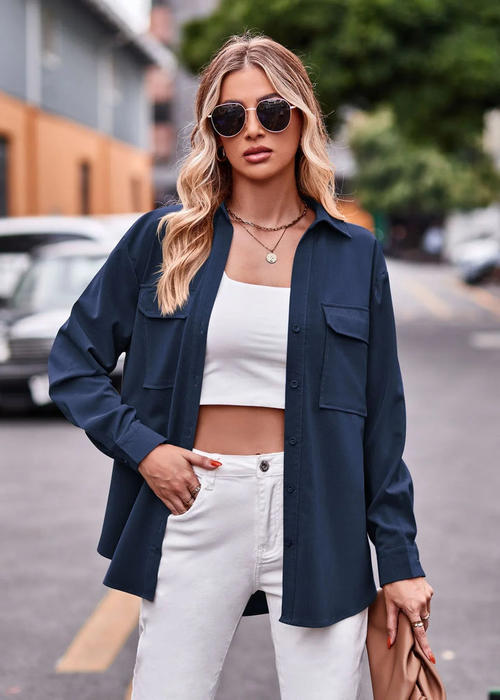 Blonde woman wearing navy shirt jacket, white crop top, white pants, and sunglasses on city street
