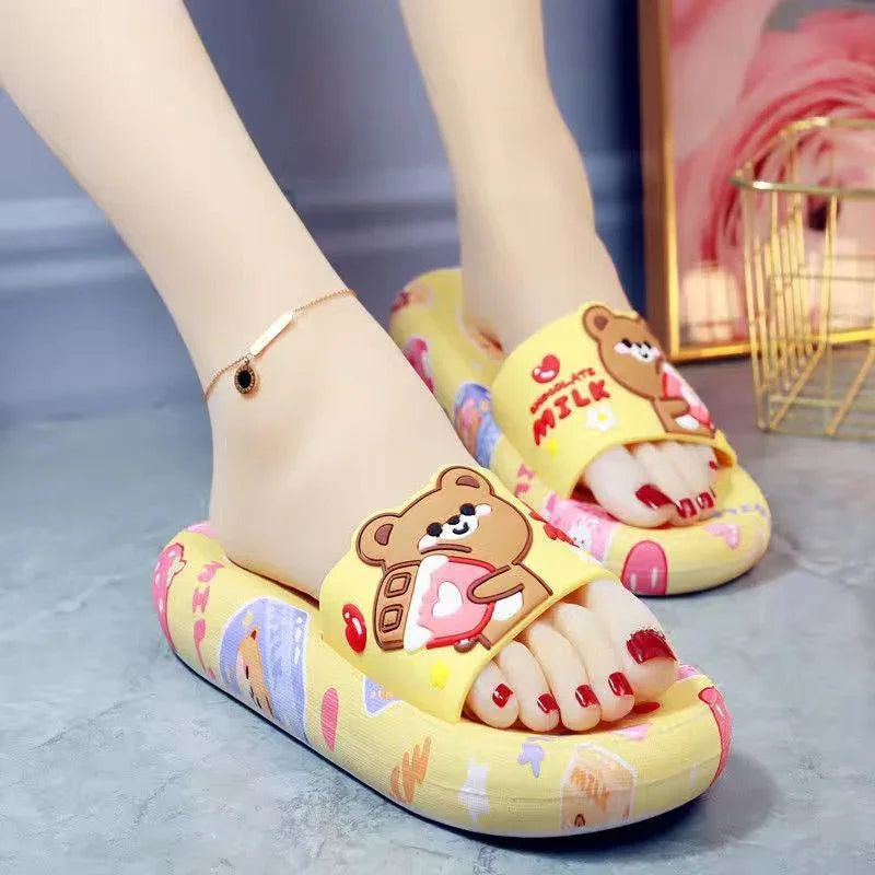 Yellow slip-on slippers with cartoon bear holding milk bottle, worn with red nail polish and ankle bracelet