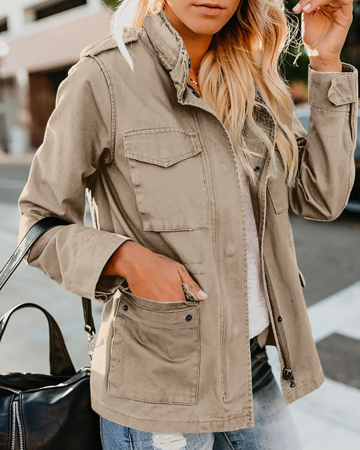 Woman wearing a beige utility jacket with four pockets, jeans, and carrying a black leather bag outdoors