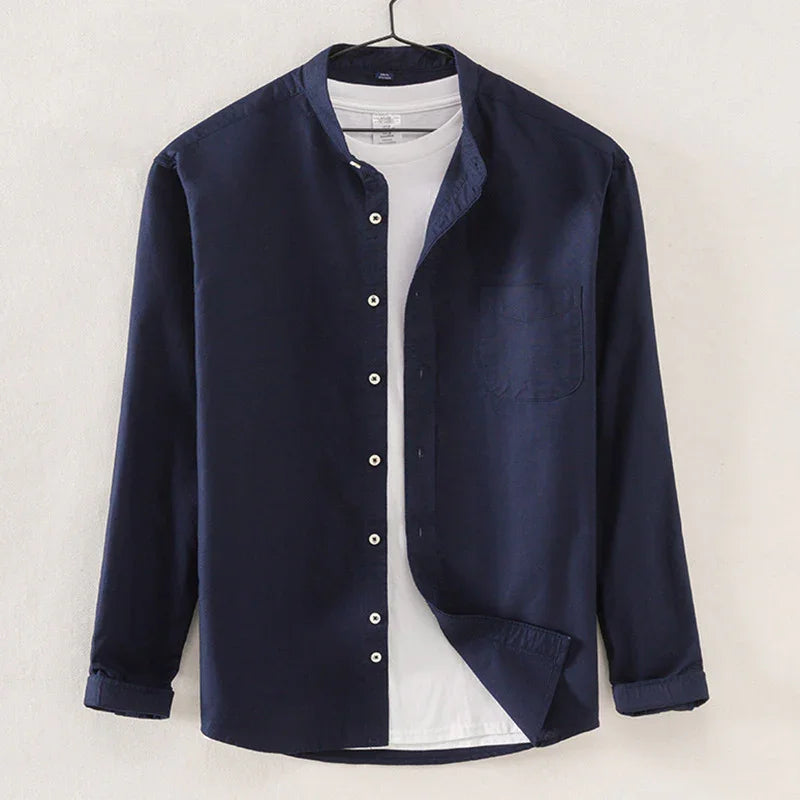 Navy blue button-up shirt over white t-shirt hanging on hanger against white wall