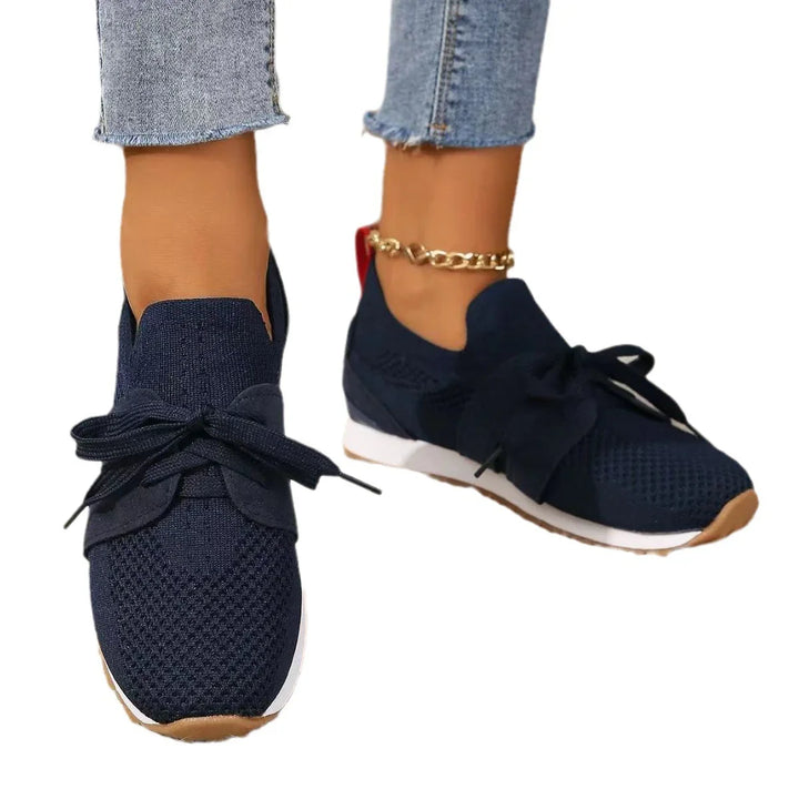 Close-up of feet wearing navy blue knit sneakers with white soles and denim jeans