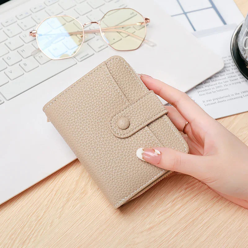 Hand holding beige textured leather wallet with snap button on wooden desk near keyboard and gold frame glasses