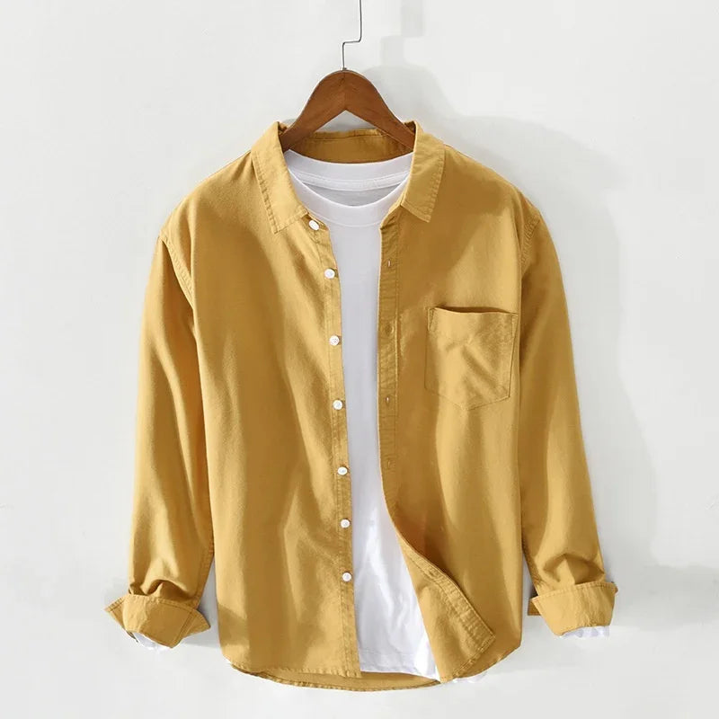 Yellow casual button-up shirt layered over white t-shirt on wooden hanger against white wall