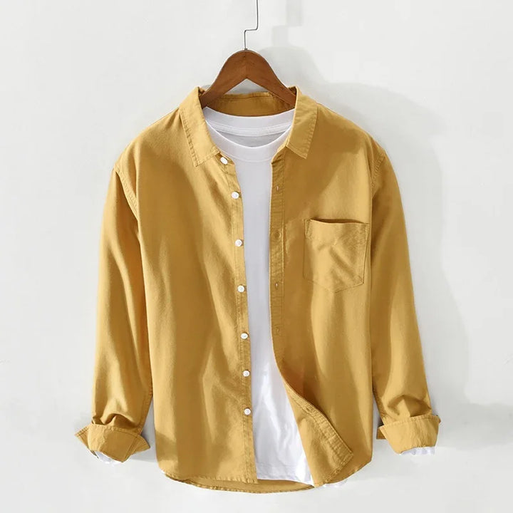 Yellow casual button-up shirt layered over white t-shirt on wooden hanger against white wall