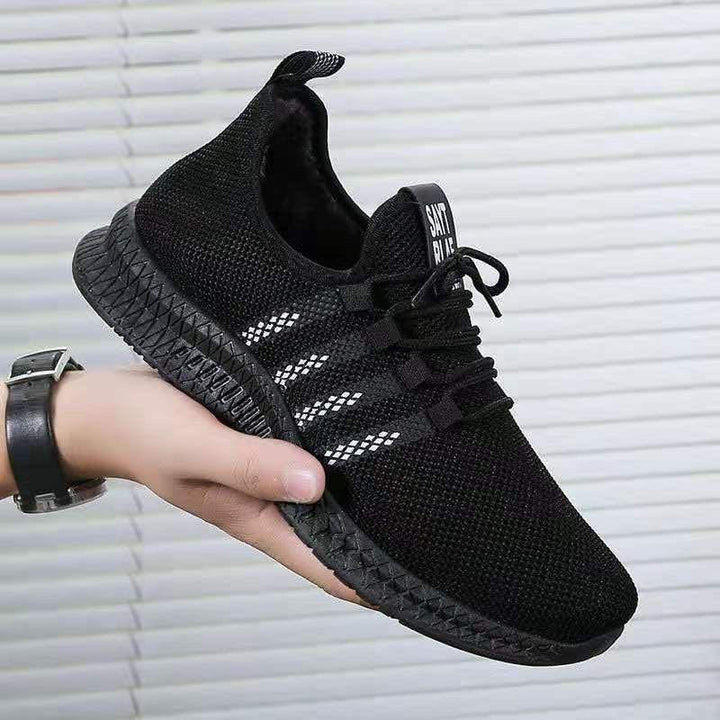 Hand holding black knit sports sneaker with white stripes and textured sole against gray background