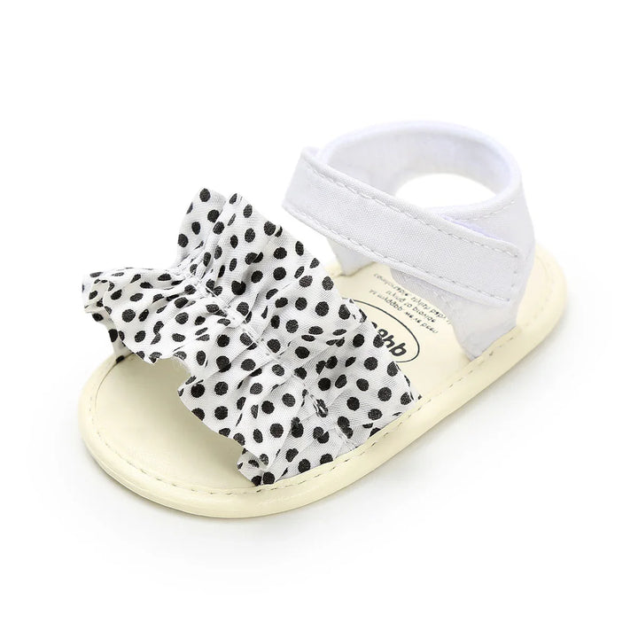 White baby sandal with black polka dot fabric bow and velcro strap on white background