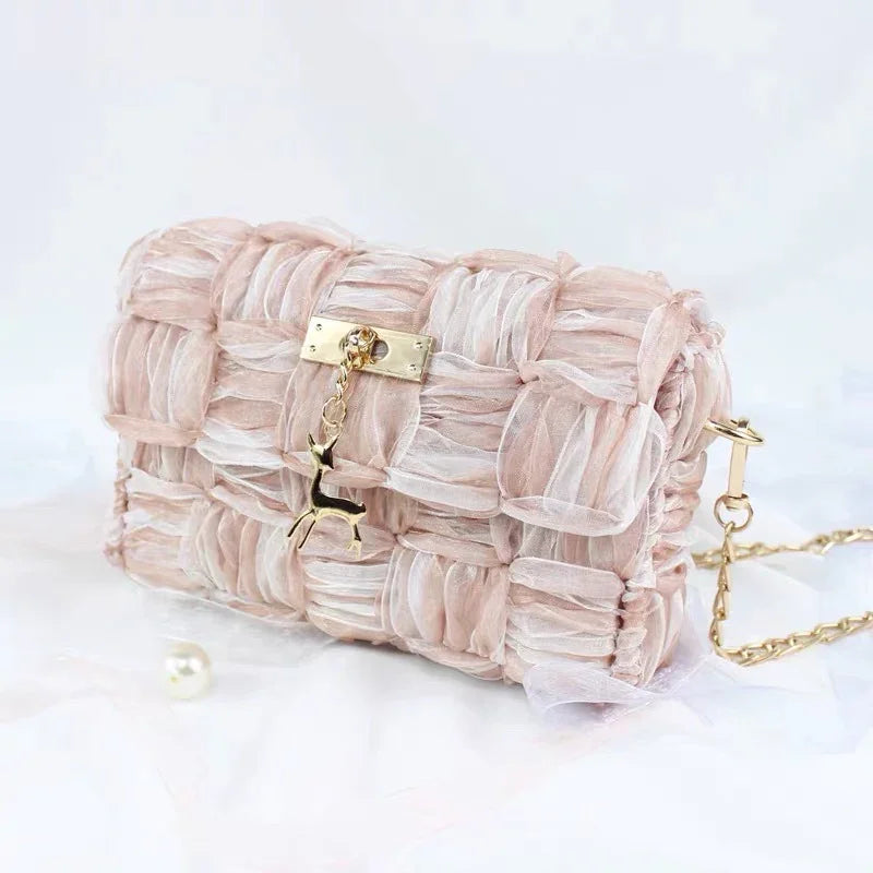Elegant pink woven fabric handbag with gold deer charm and chain strap on white background