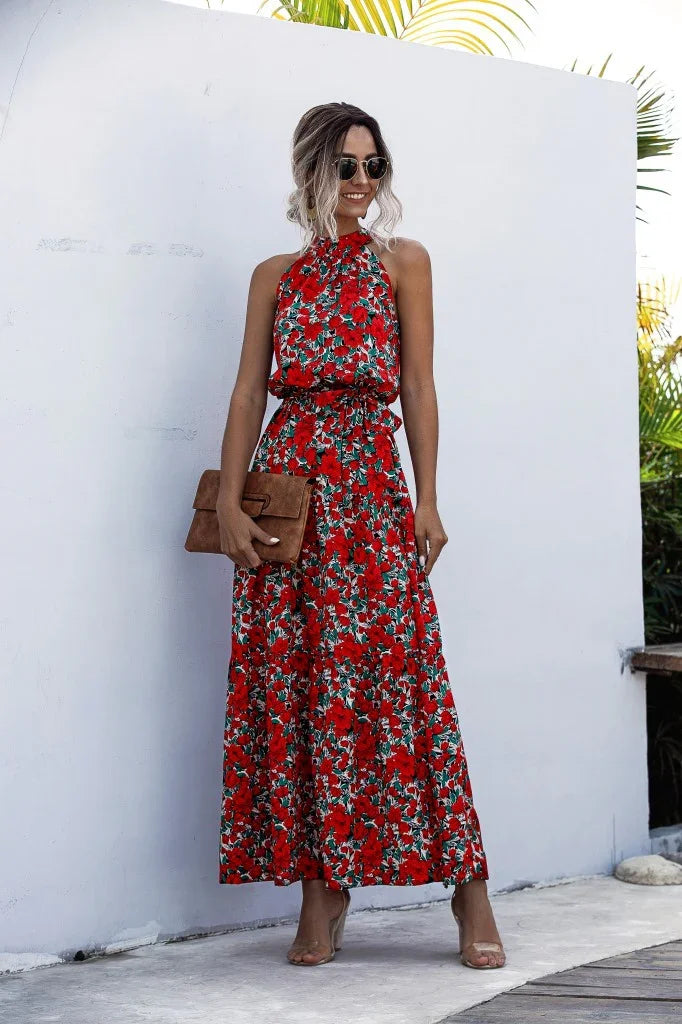 Woman wearing a red floral halter neck maxi dress holding a brown clutch purse, standing outdoors
