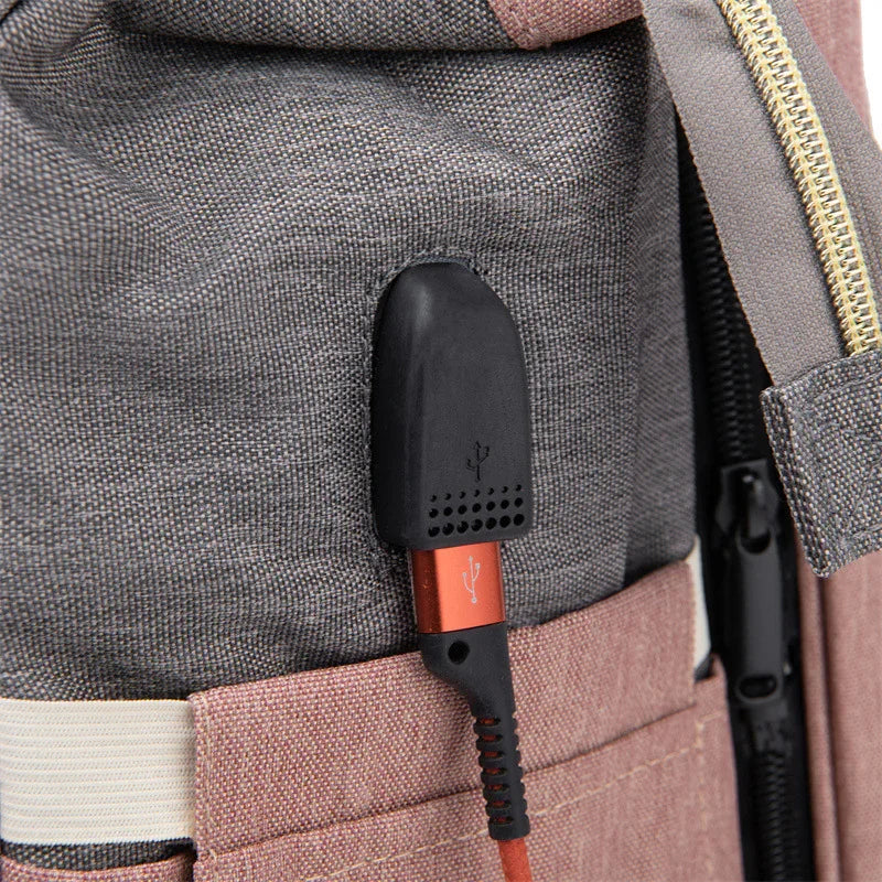 Close-up of USB charging port and red cable on grey and pink fabric backpack with zipper