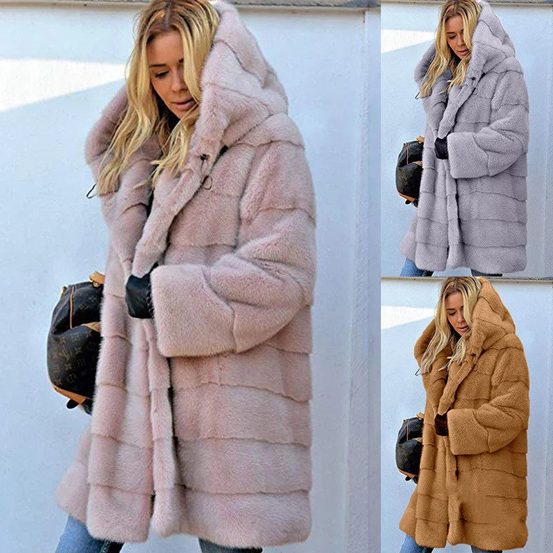Woman wearing oversized hooded faux fur coat in blush pink, gray, and camel colors, holding black handbag