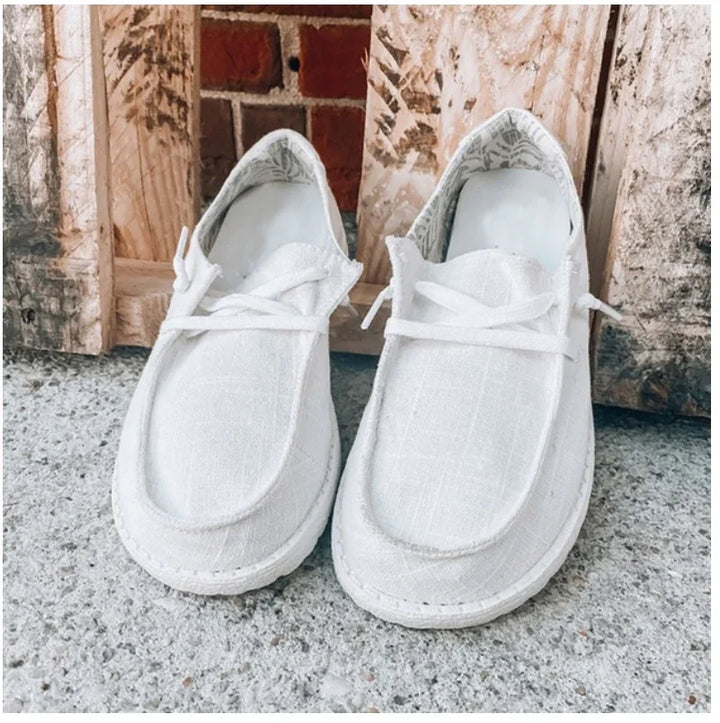 Pair of white casual lace-up shoes on a concrete floor with wooden crates in the background
