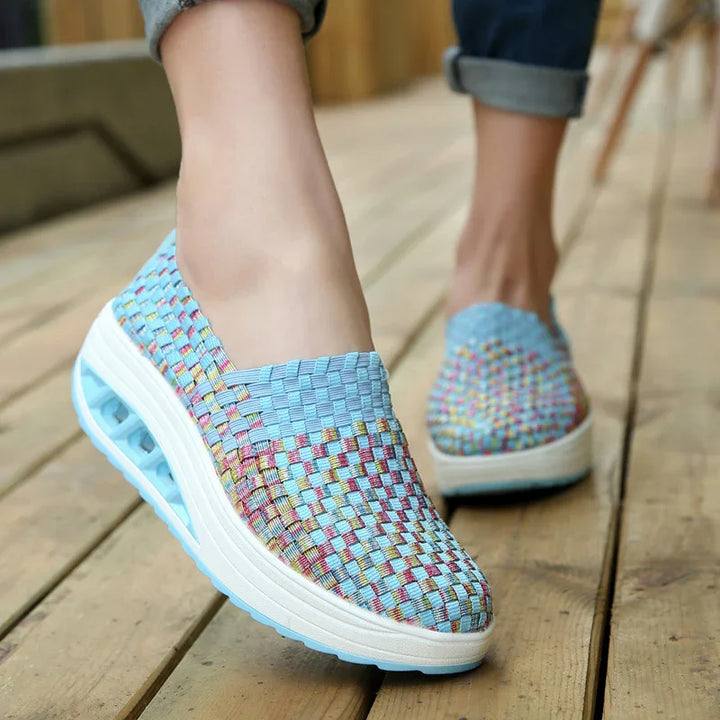 Close-up of feet wearing colorful woven slip-on platform shoes on wooden floor