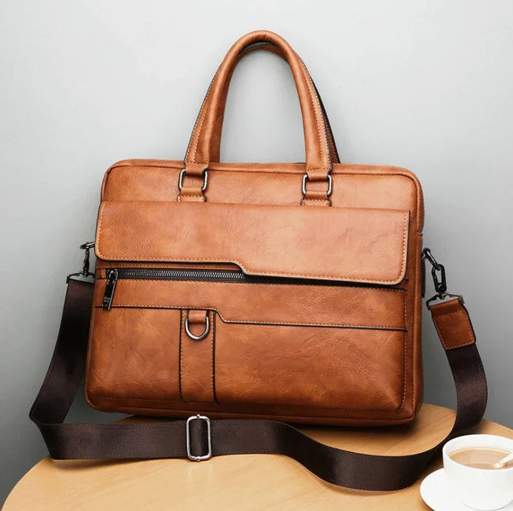 brown leather briefcase with handles and adjustable shoulder strap on wooden table