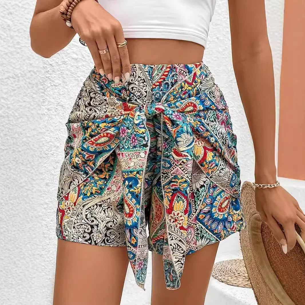 Woman wearing colorful paisley print high-waisted shorts with tie front, white crop top, and accessories