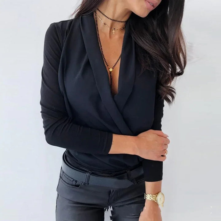 Woman wearing black long sleeve wrap top with layered necklaces and gold watch against white background