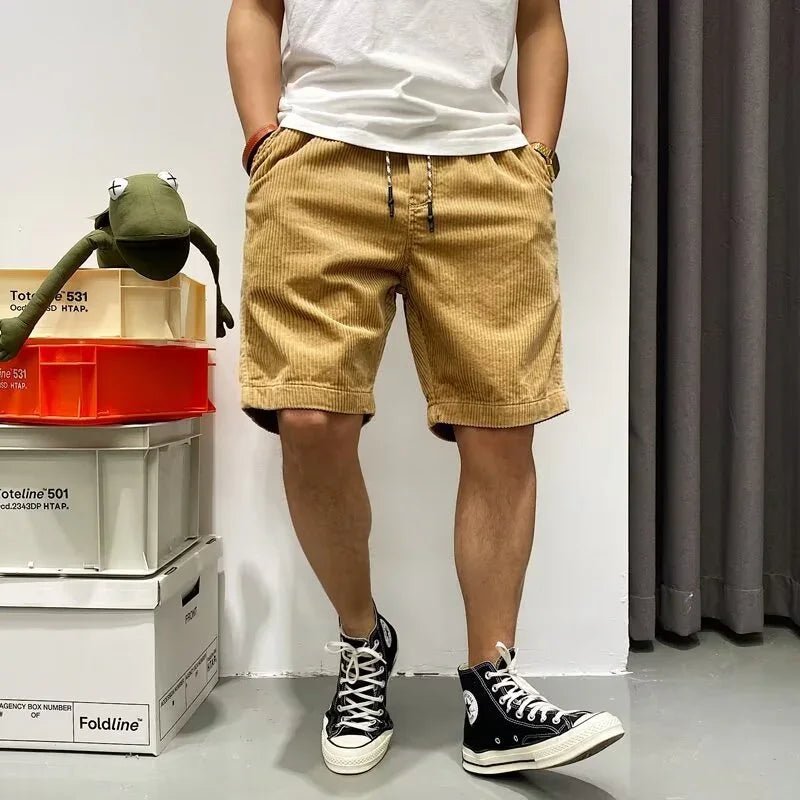 Man wearing tan corduroy shorts, white t-shirt, and black high-top sneakers standing indoors