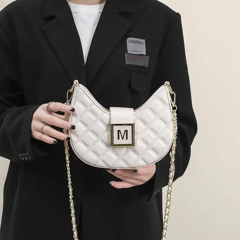 Woman in black blazer holding white quilted crescent shoulder bag with gold chain and M clasp